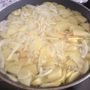 Pan met aardappelen, olie en uien dat op laag vuur zachtjes kookt 